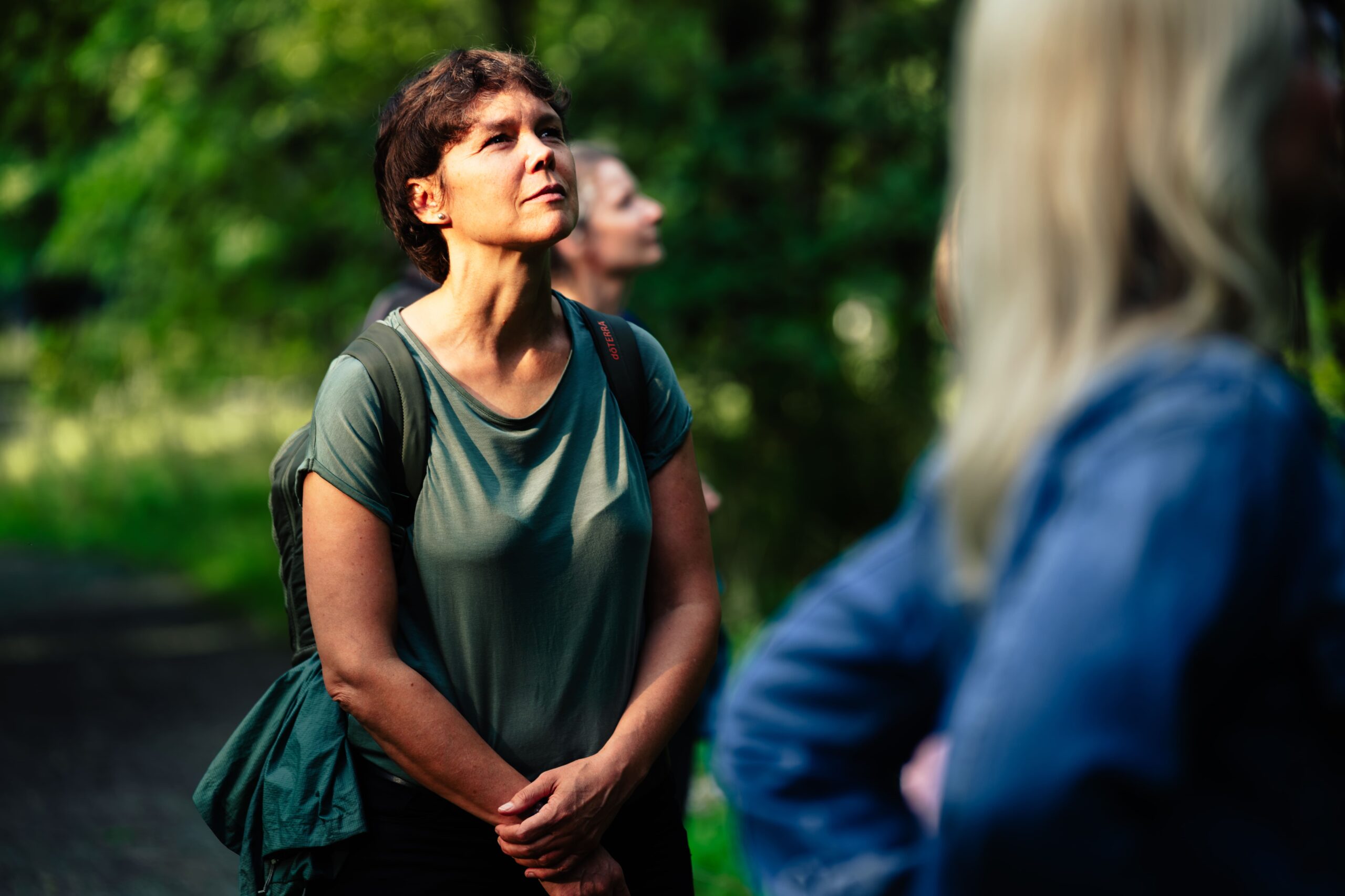 Drei Frauen stehen im Wald. Zwei im Anschnitt. Die dritte schaut glücklich und entspannt nach oben in die Bäume. Waldbaden in Potsdam von intogreen.events. (c)seelenherzfotografie